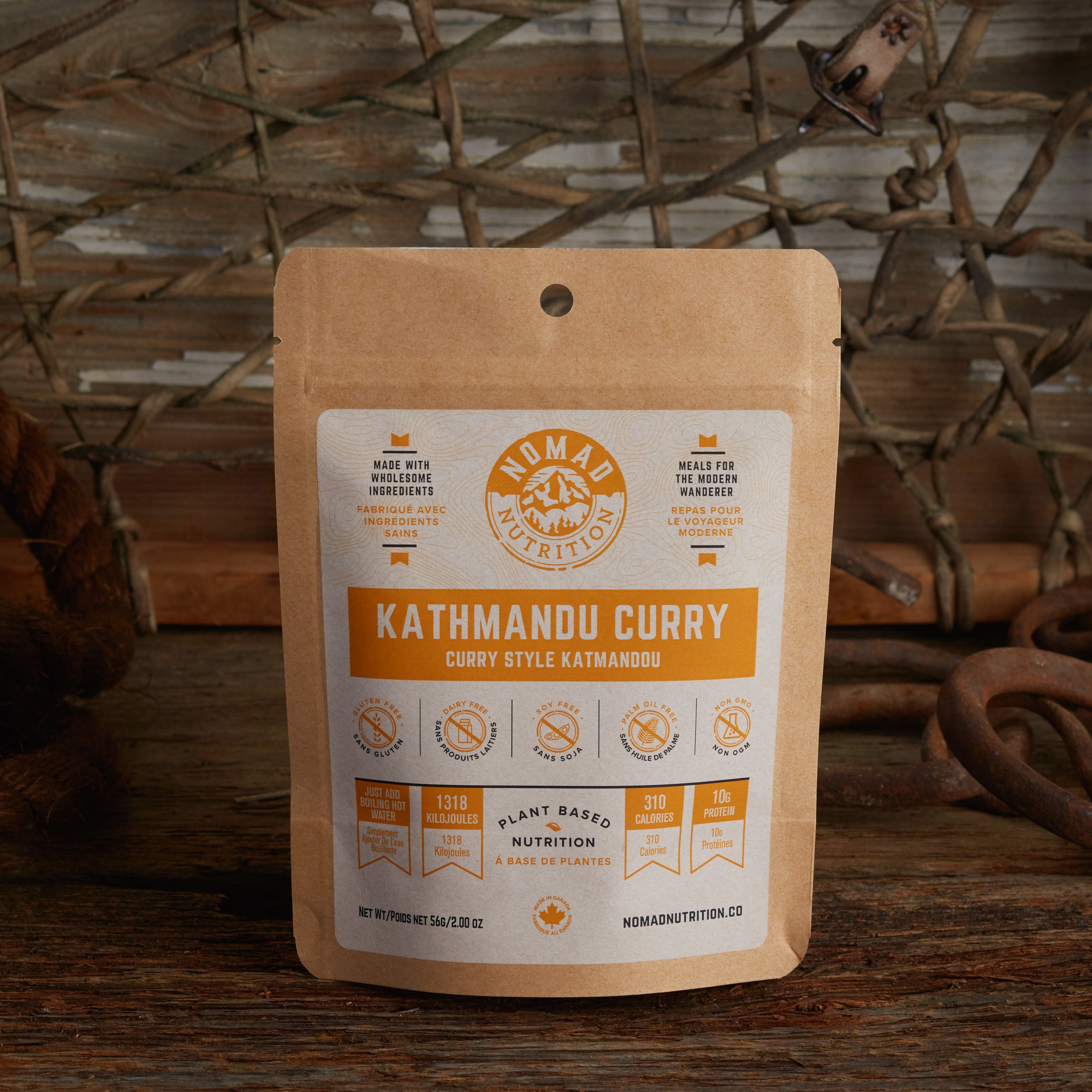 Nomad Nutrition Kathmandu Curry 56g snack size with outdoor equipments on table top.