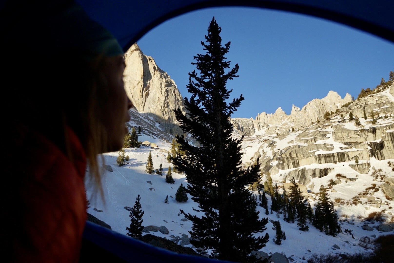 Woman looking out of tent overlooking snow-capped mountains | Avalanche safety blog