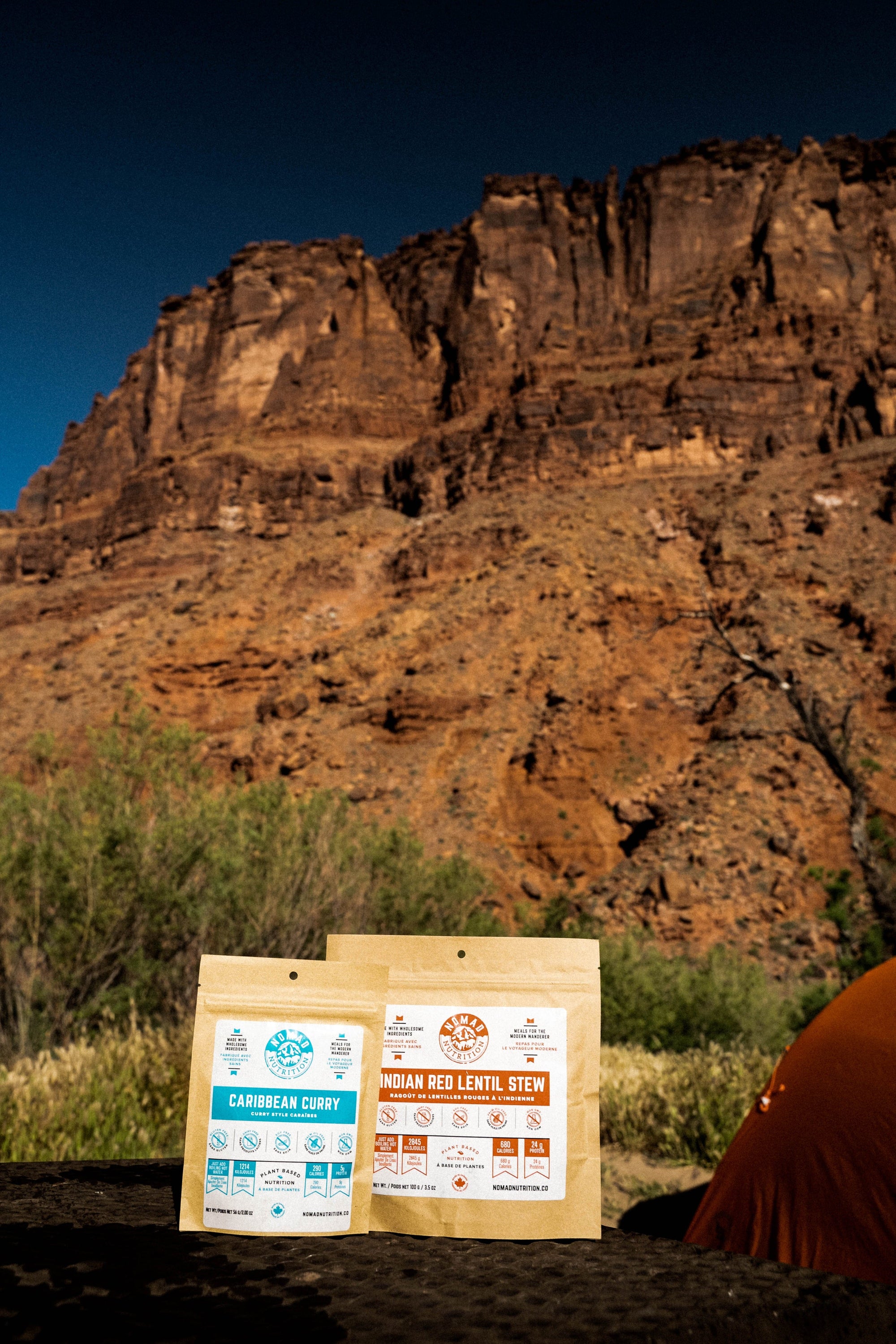 Nomad Nutrition Carribean Curry (56g/ 2oz) and Indian Red Lentil Stew (112g/ 4oz), dehydrated vegan adventure plant-based, gluten-free meal at Arches National Park with canyons visible in the background.