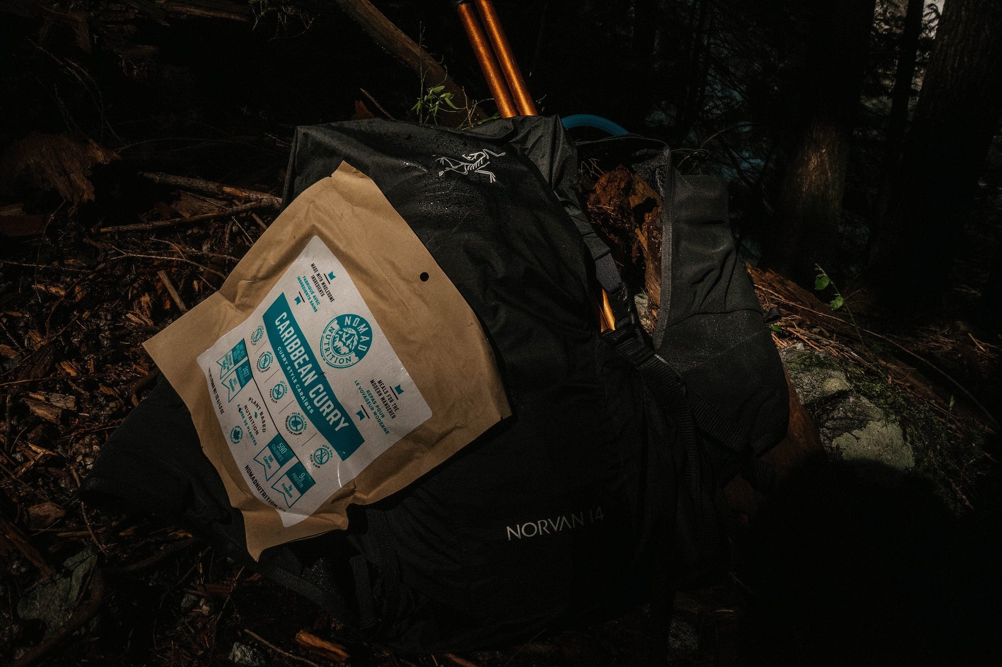 Nomad Nutrition Carribean Curry, vegan dehydrated, gluten-free, plant-based adventure meal pictured with bagpack and trekking poles for an outdoor hiking activity.