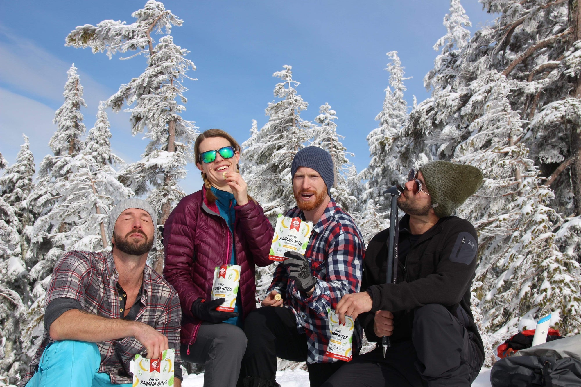 4 people posing with Nomad Nutrition's Chewy Banana Bites while enjoying the dehydrated banana pieces outdoors in the winter. 