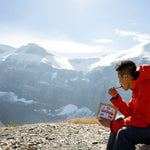 Man eating Nomad Nutrition Hungarian Goulash (112g/ 4oz), a dehydrated, vegan, adventure, plant-based, gluten-free meal outdoors overlooking the snowy mountains. 
