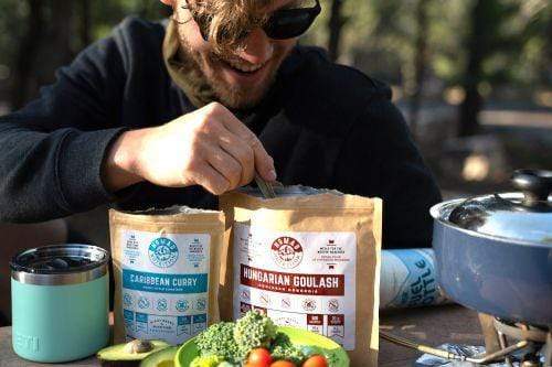 Man enjoying Hungarian Goulash 112g and Caribbean Curry 56g outdoors as camping meals.