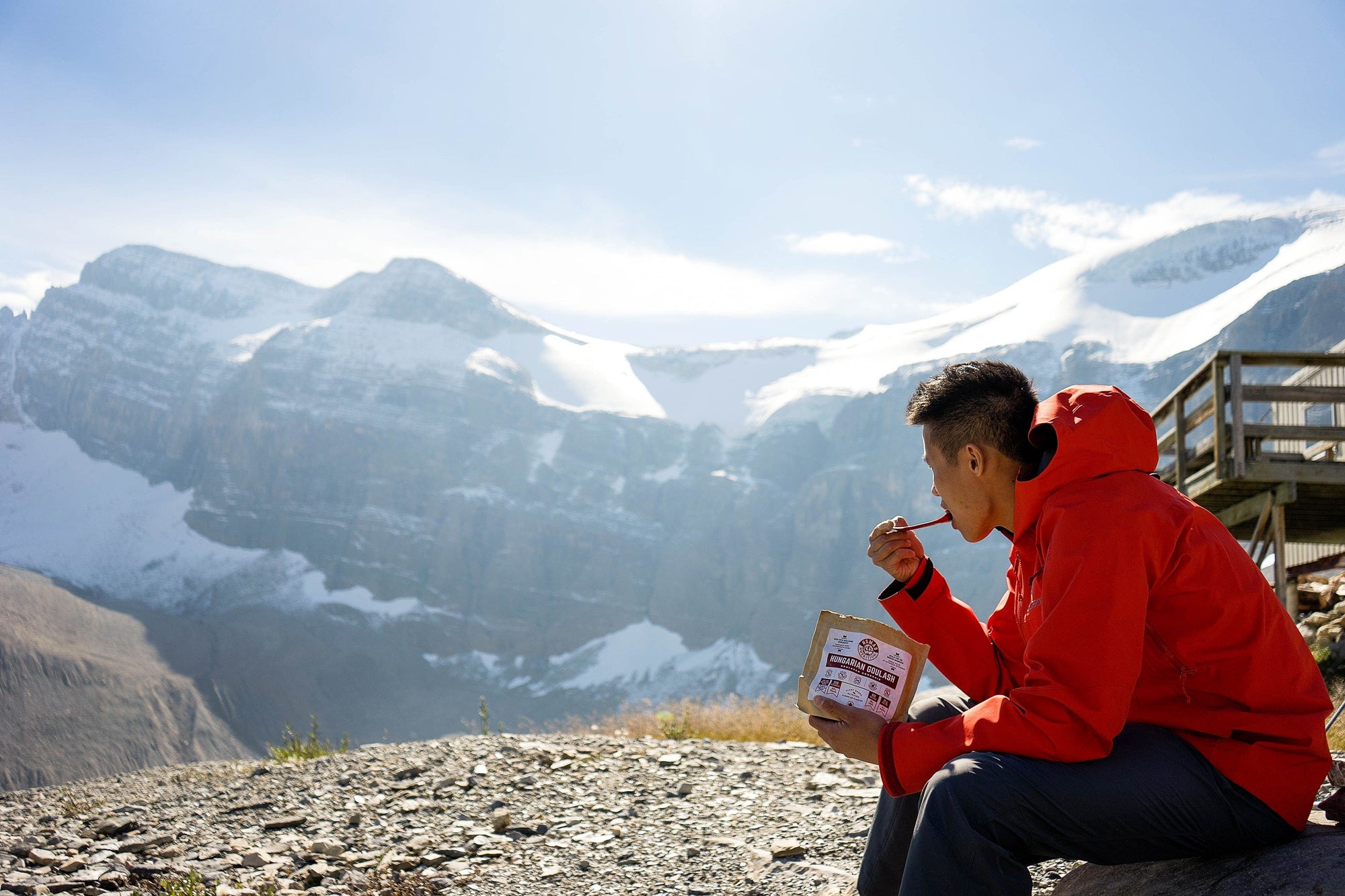Man eating Hungarian Goulash 112g meal size on top of mountain outdoors overlooking snowy mountain peaks. 