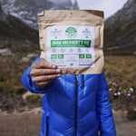 Person holding Irish Shepherd's Pie 112g/ 4oz, Person holding Irish Shepherd's Pie (112g/ 4oz), adehydrated vegan adventure plant-based, gluten-free meal outdoors surrounded by mountains. 