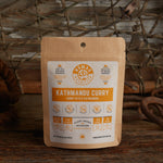 Nomad Nutrition Kathmandu Curry 56g snack size with outdoor equipments on table top.